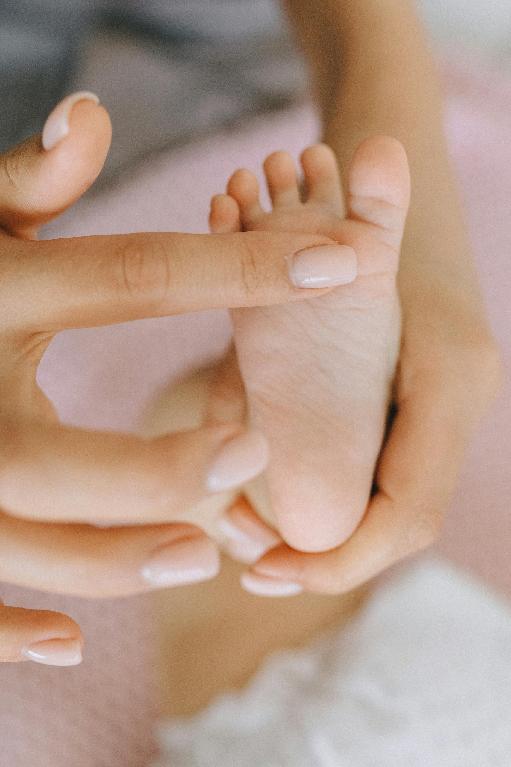 Close-up of hands gently touching a baby's foot, symbolizing care and tenderness.